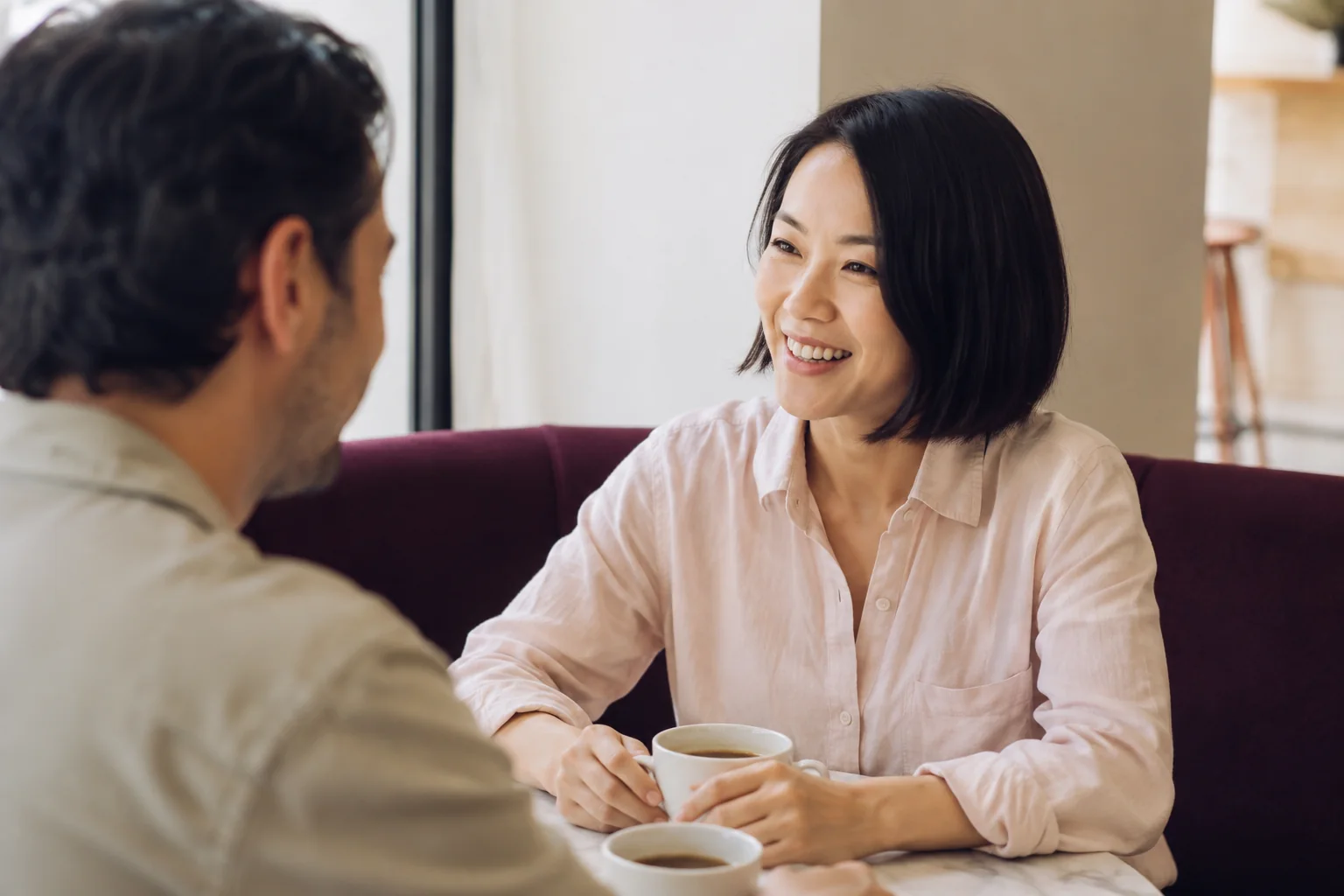 A woman smiling during a conversation with a man in a bright neighbourhood cafe.
